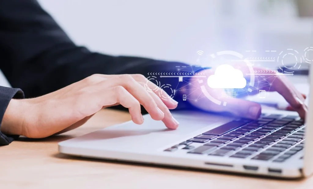 A person typing on a laptop with a digital cloud computing icon hovering above the keyboard, representing cloud technology and data storage.