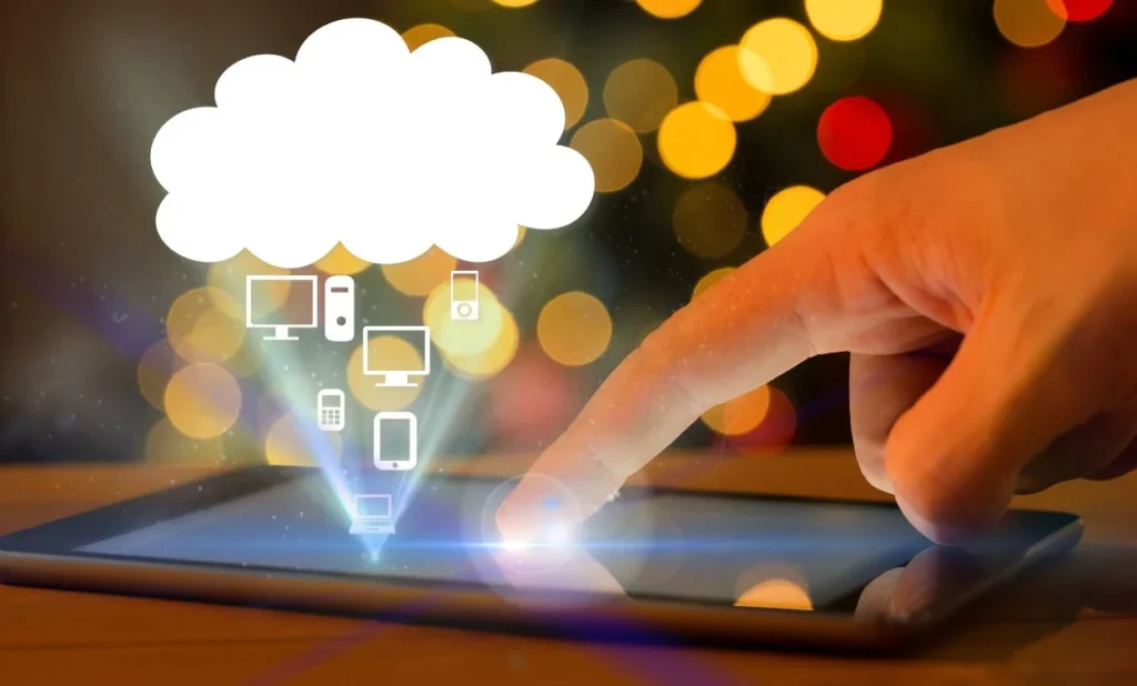 Finger touching a tablet screen with glowing icons of devices rising into a white cloud symbol, representing cloud computing and device connectivity.