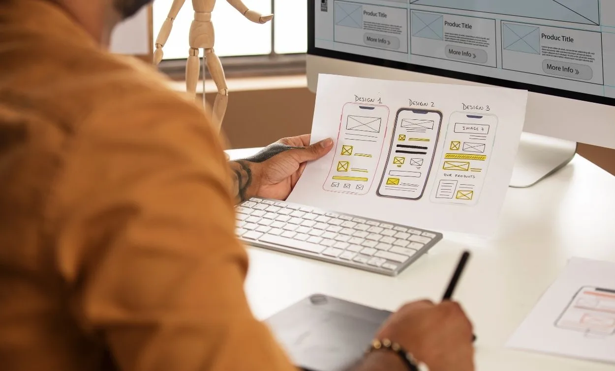 UI UX designer creating mobile app wireframes and user interface layouts on paper and computer screen