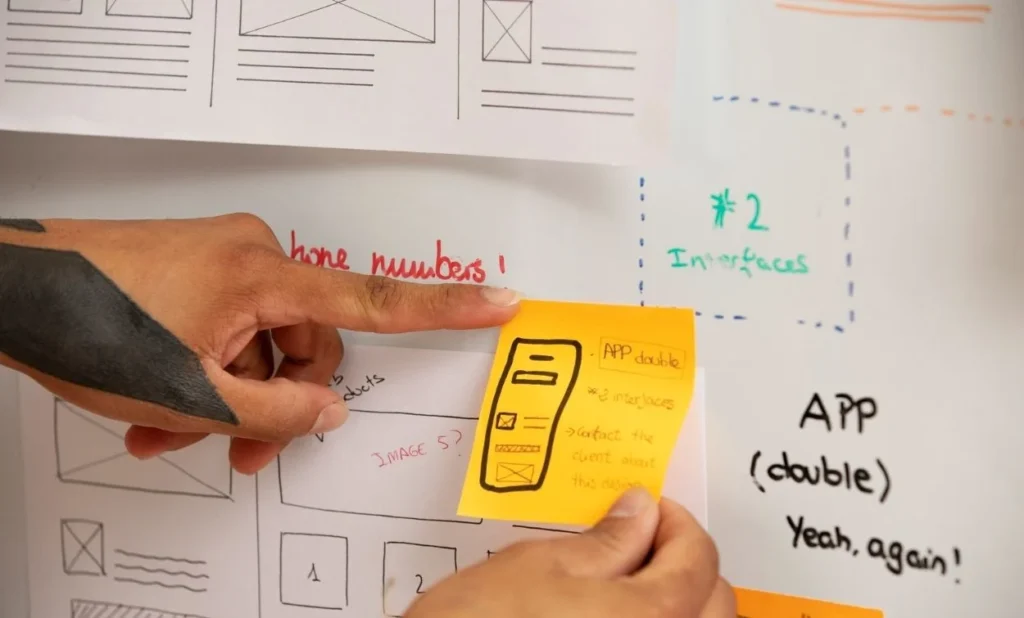 Designer creating a mobile app wireframe using sticky notes and hand-drawn UI layouts during the planning stage.