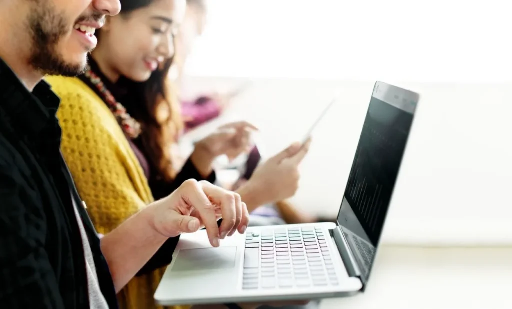 Students attending a software training session while working on laptops and digital devices in a modern classroom environment.