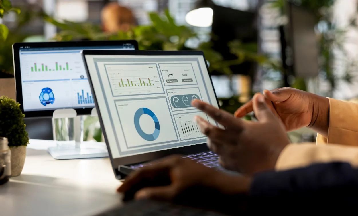 Data science professionals analyzing charts and dashboards on a laptop and monitor in an office.